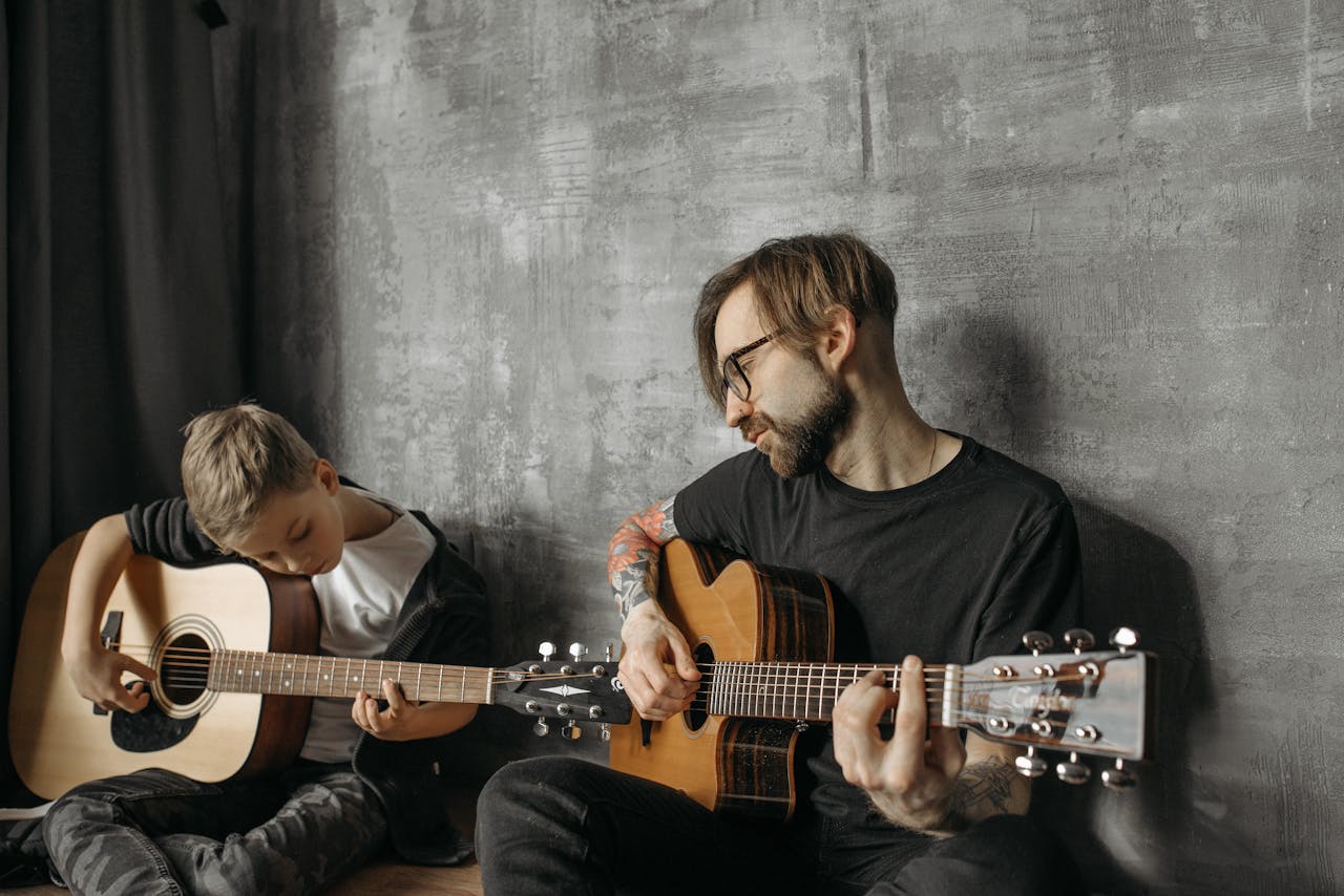 A father and son duo playing acoustic guitars together in a cozy indoor setting.